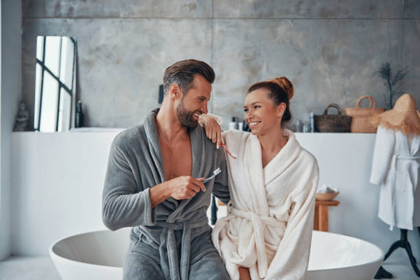 Beautiful young couple in bathrobes smiling and cleaning teeth stock photo