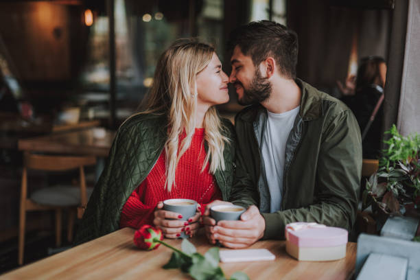 Beautiful young couple touching noses and smiling at cafe Romantic date. Charming girl and her boyfriend sitting at the table and holding cups of coffee dating stock pictures, royalty-free photos & images