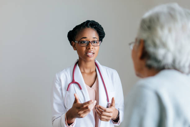 Beautiful young female doctor explaining to senior patient A beautiful young female doctor standing face to face with a senior female patient and explaining with hand gestures. beautiful haitian women stock pictures, royalty-free photos & images