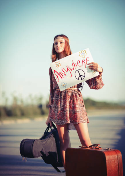 Beautiful young hippie girl hitchhiking on a road stock photo