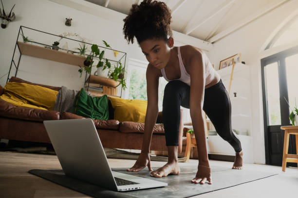 mooie jonge gemengde rasvrouw die van huis, online training op laptop uitwerkt - fitness stockfoto's en -beelden