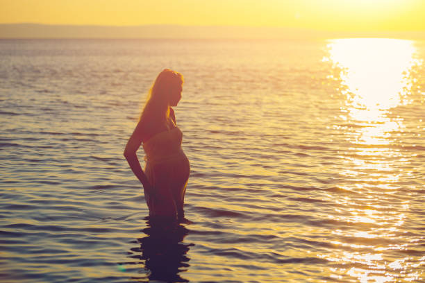 Beautiful young pregnant woman playing with water at the sea in the summer at sunset Concept Love and pregnancy stock photo