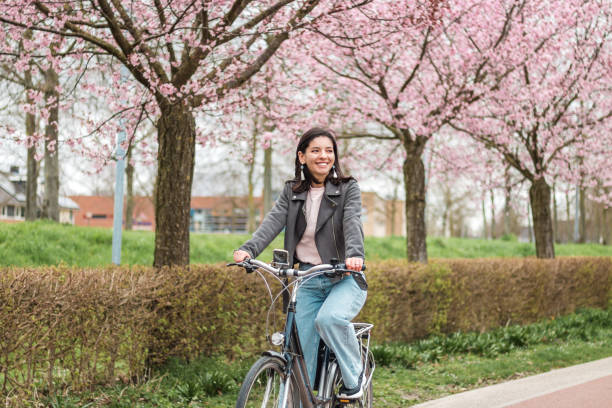 mooie jonge vrouw van gemengde rassenminderheid die op fiets in bloeiende lente in toevallige kleren met aantrekkelijke glimlach berijdt. lifestyle recreatief portret - fietsen stockfoto's en -beelden