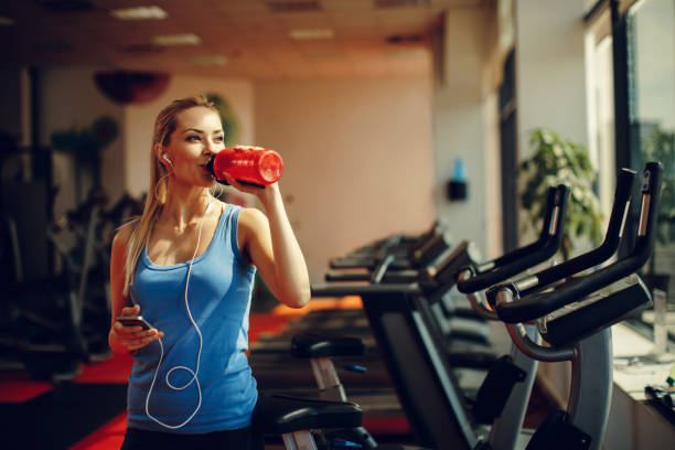 Beautiful young woman resting and drinking water in the gym stock photo