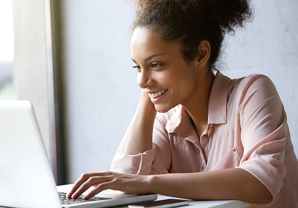 Beautiful young woman smiling and looking at laptop screen Close up portrait of a beautiful young woman smiling and looking at laptop screen side view photos stock pictures, royalty-free photos & images
