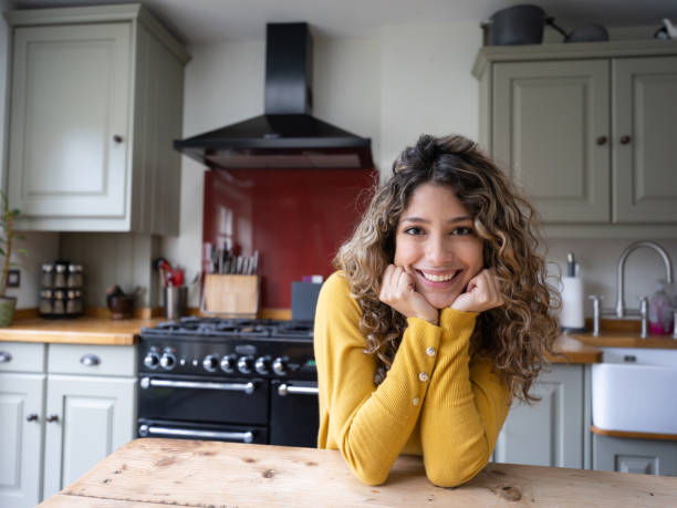 bella giovane donna sorridente alla macchina fotografica appoggiato gomiti sul bancone della cucina molto allegramente - fotografia immagine foto e immagini stock
