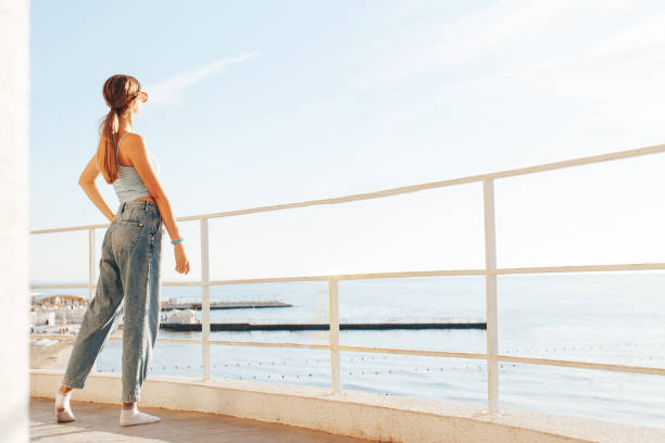 beautiful young woman standing on the balcony morning  and looking at the sea. Woman look at the sea on terrace. Back view stock photo