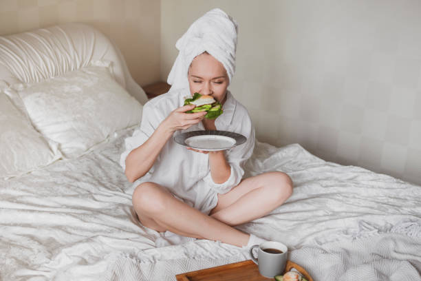 beautiful young woman with a towel on her head in bed eating healthy breakfast stock photo