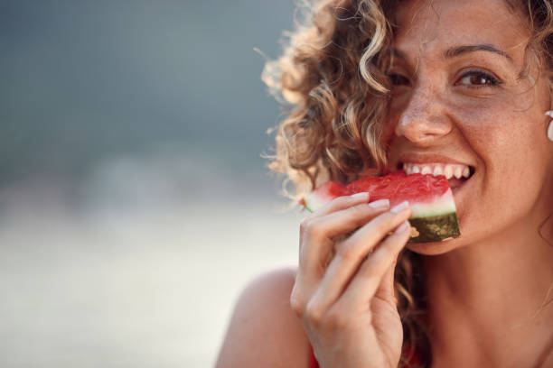 Beautiful young woman with curly hair biting on watermelon piece. Summertime, holiday, lifestyle concept. stock photo