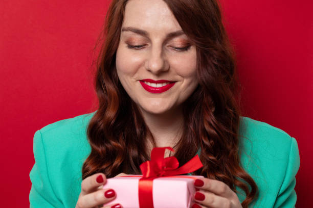 vacker ung kvinna med uttrycker glada känslor och håller presentbox på en röd vägg bakgrund. - santa holding magazine bildbanksfoton och bilder