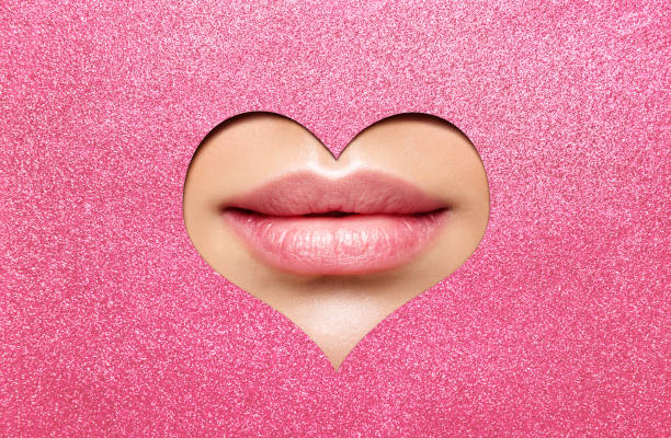 Beauty Lips Makeup Close up. Natural Plump Bright Lip Glossy Lipstick look through Heart Shaped Hole in Pink Glitter Paper. Lips Cosmetic, Blushing, Cosmetology Surgery stock photo
