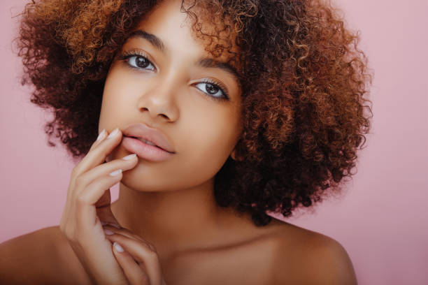 Beauty portrait of a beautiful African American young woman with a mysterious look at the camera and putting her fingers to her face stock photo