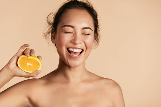 Beauty. Smiling woman with radiant face skin and orange portrait Beauty. Smiling woman with radiant face skin and orange portrait. Beautiful smiling asian girl model with natural makeup, healthy smile and glowing hydrated facial skin. Vitamin C cosmetics concept healthy skin stock pictures, royalty-free photos & images