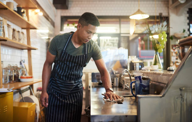 Because you can't work in a messy place Shot of a young man cleaning a countertop in a cafe restaurant cleaning stock pictures, royalty-free photos & images