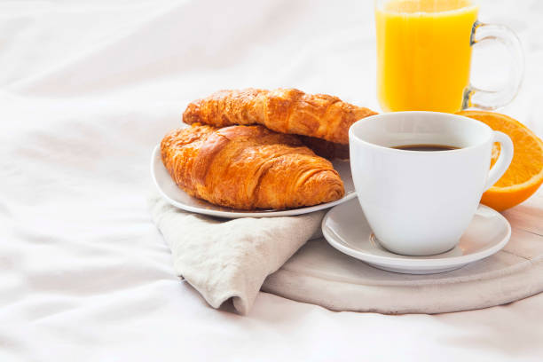 Bed breakfast with coffee cup, croissants and orange juice on white sheets stock photo
