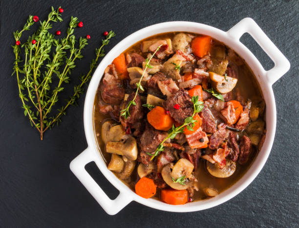 Beef Bourguignon in a casserole on black stone. Beef Bourguignon in a casserole on black stone. Stewed with bacon, garlic, carrots, onions, mushrooms,  red wine, fresh thyme and spices. Top view. casserole dish stock pictures, royalty-free photos & images