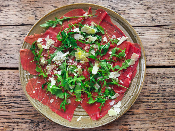 Beef carpaccio raw meat slices served on a dish against wooden background. stock photo