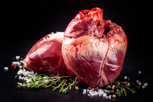 Beef raw heart on a black background with rosemary and spices. stock photo