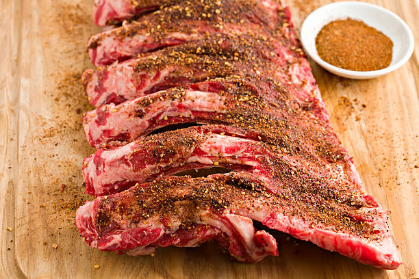 Beef Ribs And Dry Rub "A high angle view of a slab of beef ribs with a bowl of spicy,Texas style dry rub lying on a wooden cutting board." rubbing stock pictures, royalty-free photos & images