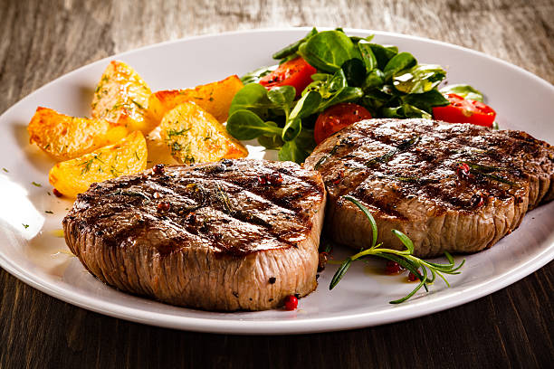 beef steaks, baked potatoes and vegetable salad - biefstuk stockfoto's en -beelden