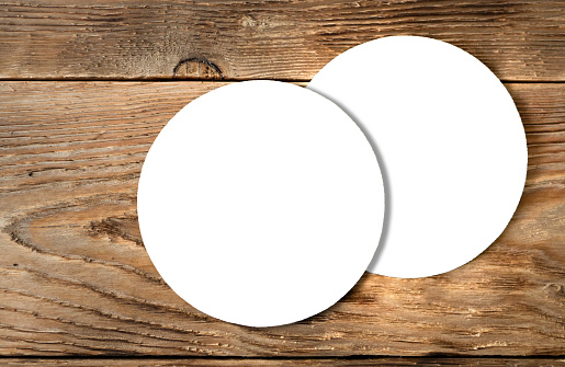 White coasters isolated on wooden background. Ready mock up of blank round mat for brewery design, advertising, brand representing