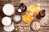 Beer in bottles and glasses on a wooden table. Beer and snacks are pistachio nuts, chips and nachos top view. Drink and snack for the football match or party"n