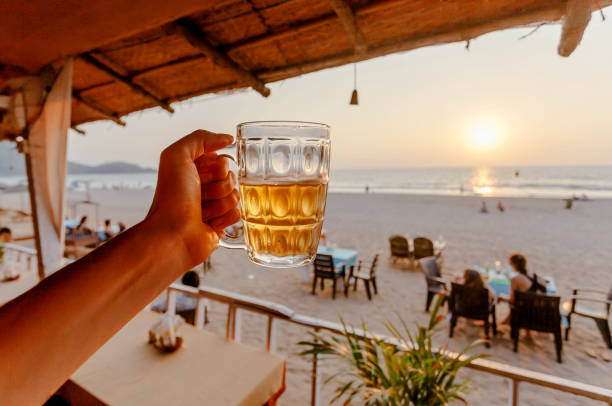 Beer mug in hand of tourist relaxing on a beach with lounge and some cafe outdoor of Asia stock photo