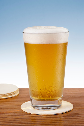 A refreshing pint of cold beer sitting on a bar coaster with a gradated blue background.