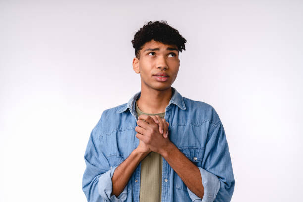 Begging young mixed-race man in casual outfit isolated over white background  prayer request stock pictures, royalty-free photos & images