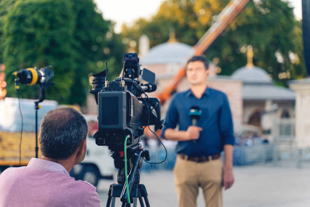 Behind the scene concept. Cameraman working on professional camera taking TV interviewer, professional news reporter making news outdoors. stock photo
