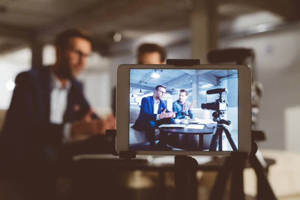 Behind the scenes of a business vlog Two bloggers on digital tablet screen. Businessman with male guest recording a video blog on camera. Behind the scenes of a business vlog. vlogging stock pictures, royalty-free photos & images