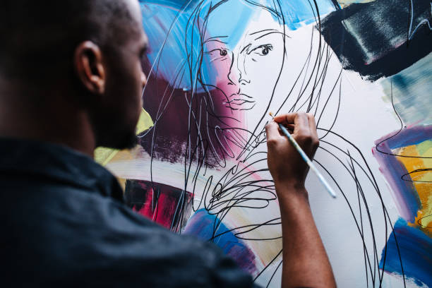 Behind view of a black man painting on an easel, applying colour stock photo