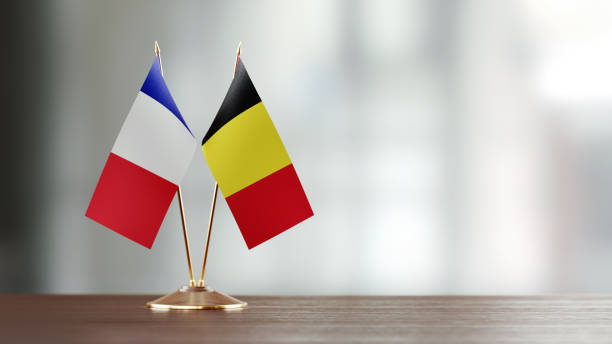 Belgian flag and French flag pair on desk over defocused background. Horizontal composition with copy space and selective focus.