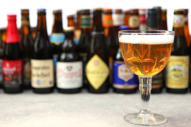 Belgian Beer Glass and Variety of Bottles in the Background A full glass of Belgian abbey beer is standing in front of many different types of Belgian beer bottles against white background. The bottles in the background are blur, providing space for text. belgian culture stock pictures, royalty-free photos & images