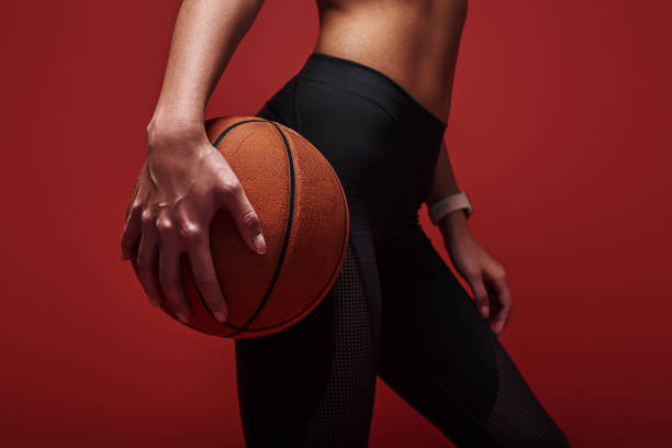 geloof het, het bereiken van jonge sportsvrouw bedrijf basketbal bal, staande over rode achtergrond - basketball player back stockfoto's en -beelden