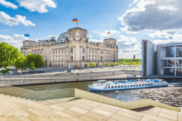 Berlin government district with Reichstag and ship on Spree river in summer, Berlin Mitte, Germany Panoramic view of Berlin government district with excursion boat on Spree river passing famous Reichstag building and Paul Lobe Haus on a sunny day with blue sky and clouds, Berlin Mitte, Germany cupola stock pictures, royalty-free photos & images