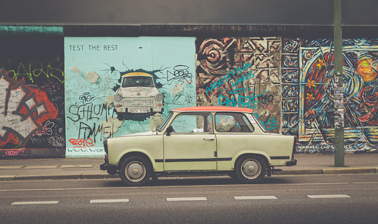 Berlin, Germany - July 12, 2015: Famous Berliner Mauer (Berlin Wall) at East Side Gallery with an old Trabant, the most common vehicle used in East Germany, in front, Berlin Friedrichshain-Kreuzberg, Germany.