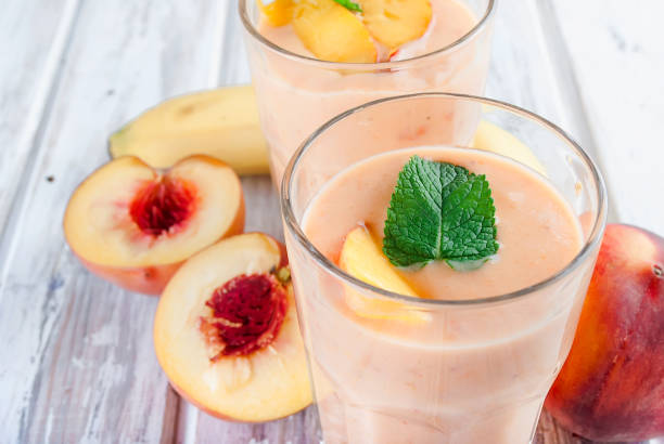 Berry smoothies of apricot, peach and banana  in glasses and ingredients on a wooden table refreshing Summer smoothie or milkshake with apricot, peach and banana, mint, yogurt in glass with ingredients, on white wooden table, copy space, peach smoothie stock pictures, royalty-free photos & images