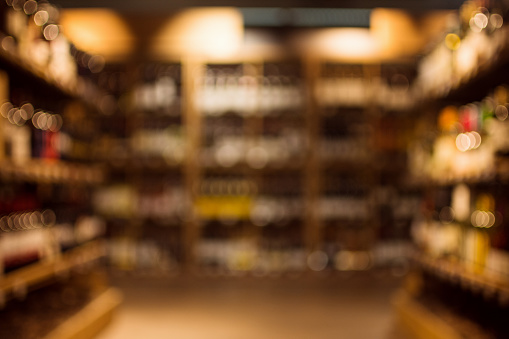Different beverages are on shelves in illuminated drink store, blurred or defocused background.