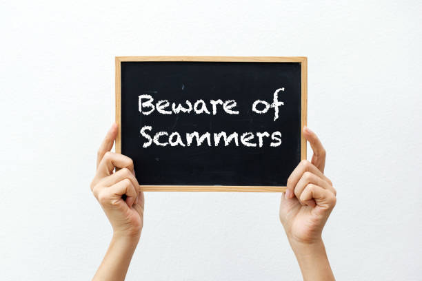 Beware of Scammers Sign Cropped hands holding a chalkboard with "Beware of Scammers" against a white background scammer stock pictures, royalty-free photos & images