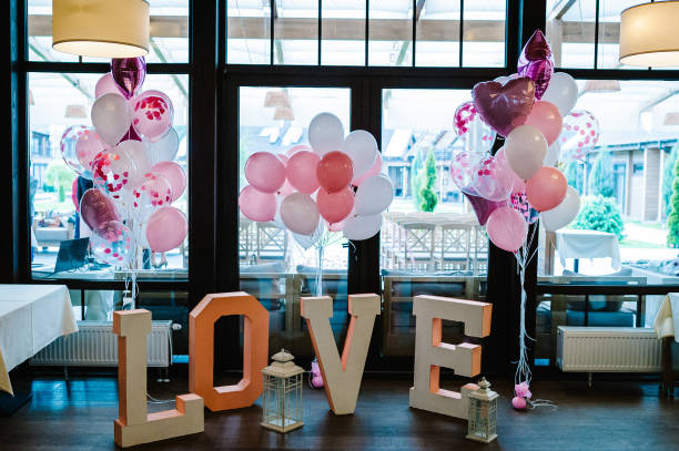 Big decorated letters Love and inflatable pink and white balls with helium are on a wooden floor in a restaurant in the area for the wedding ceremony. Photo Zone on day of lovers and valentines day. Big decorated letters Love and inflatable pink and white balls with helium are on a wooden floor in a restaurant in the area for the wedding ceremony. Photo Zone on day of lovers and valentines day. nn girls stock pictures, royalty-free photos & images