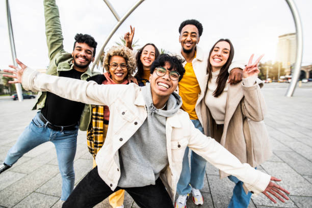 Big group of happy friends stands together on city street with raised arms - Multiracial young people having fun outside - Volunteer with hands up showing teamwork spirit - Community and friendship stock photo