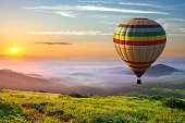 istock Big hot air baloon over idyllic landscape with green grass covered morning mountains with distant peaks and wide valley full of thick white cloudy fog. 1284120860