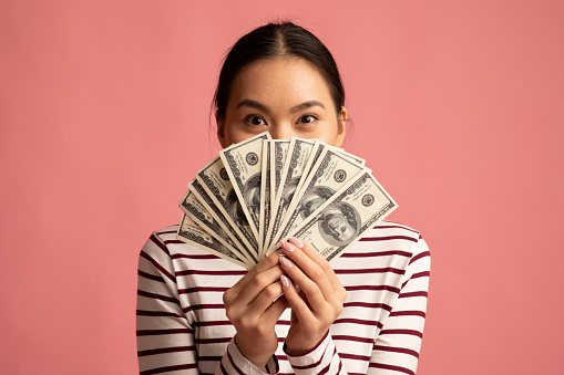 Big Profit. Happy Young Asian Woman Covering Face With Dollar Cash Fan, Lucky Millennial Korean Female Holding Lots Of Money, Gor Prize, Standing Isolated Over Pink Background, Closeup Shot