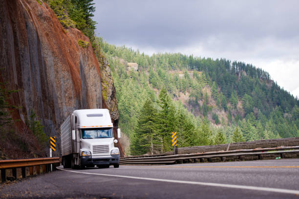 Big rig semi truck with reefer trailer transporting cargo on winding road with with a rock on one side and a precipice on the other Big rig semi truck with refrigeration trailer transporting cargo moving on the bridge on a winding road with a rock wall on one side and a precipice on the other in Columbia Gorge national park area columbia river gorge stock pictures, royalty-free photos & images