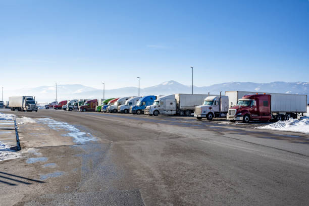 Big rig semi trucks with semi trailers standing in row on the snow and icy truck stop parking lot at winter season stock photo