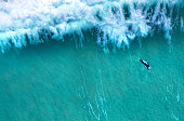 istock Big wave splashing behind a lonely surfer seen from above 1364583477