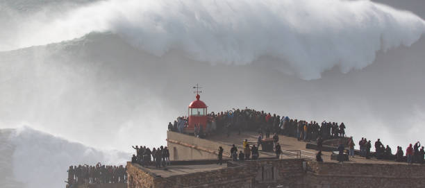 Biggest Wave In The World, Nazare, Portugal Stunning Image of giant wave crashing into cliff and lighthouse  after major Atantic Storm. big wave surfing stock pictures, royalty-free photos & images