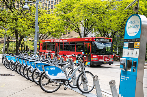 Pittsburgh, Pennsylvania, USA- May 12, 2021: Healthy Ride bike share station with red public bus passing in the background.