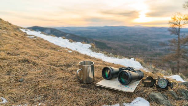 Binoculars map compass and mug on the background of nature mountains in the sunset. stock photo
